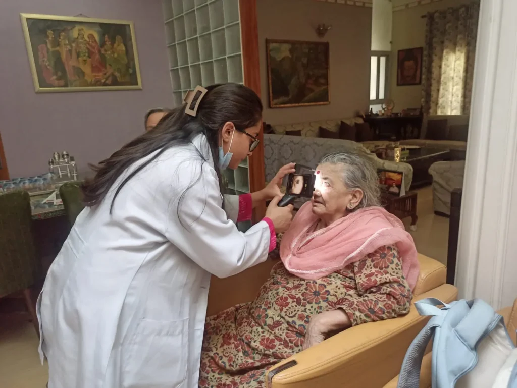 Doctor examining an elderly woman's eyes with a handheld device in her living room