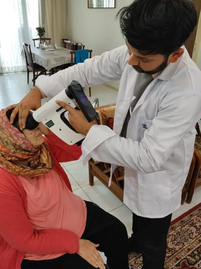 Optometrist using a handheld retinal camera on an elderly patient